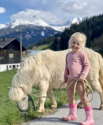 Ein kinderfreundliches Erlebnis auf dem Bauernhof mit einem sanften Pony vor einer malerischen Bergkulisse.