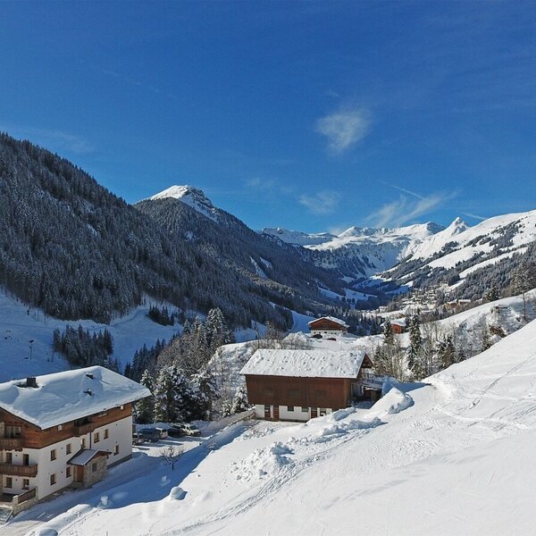Der Bauernhof im Winter, direkt an der Skipiste gelegen, mit Blick auf das Tal und die umliegenden schneebedeckten Berge.