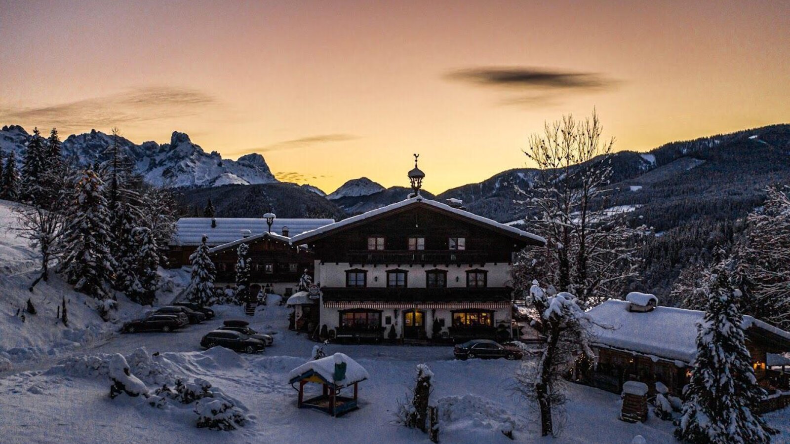 Der Bauernhof in verschneiter Winterlandschaft mit den Salzburger Dolomiten im Hintergrund bei Sonnenuntergang.