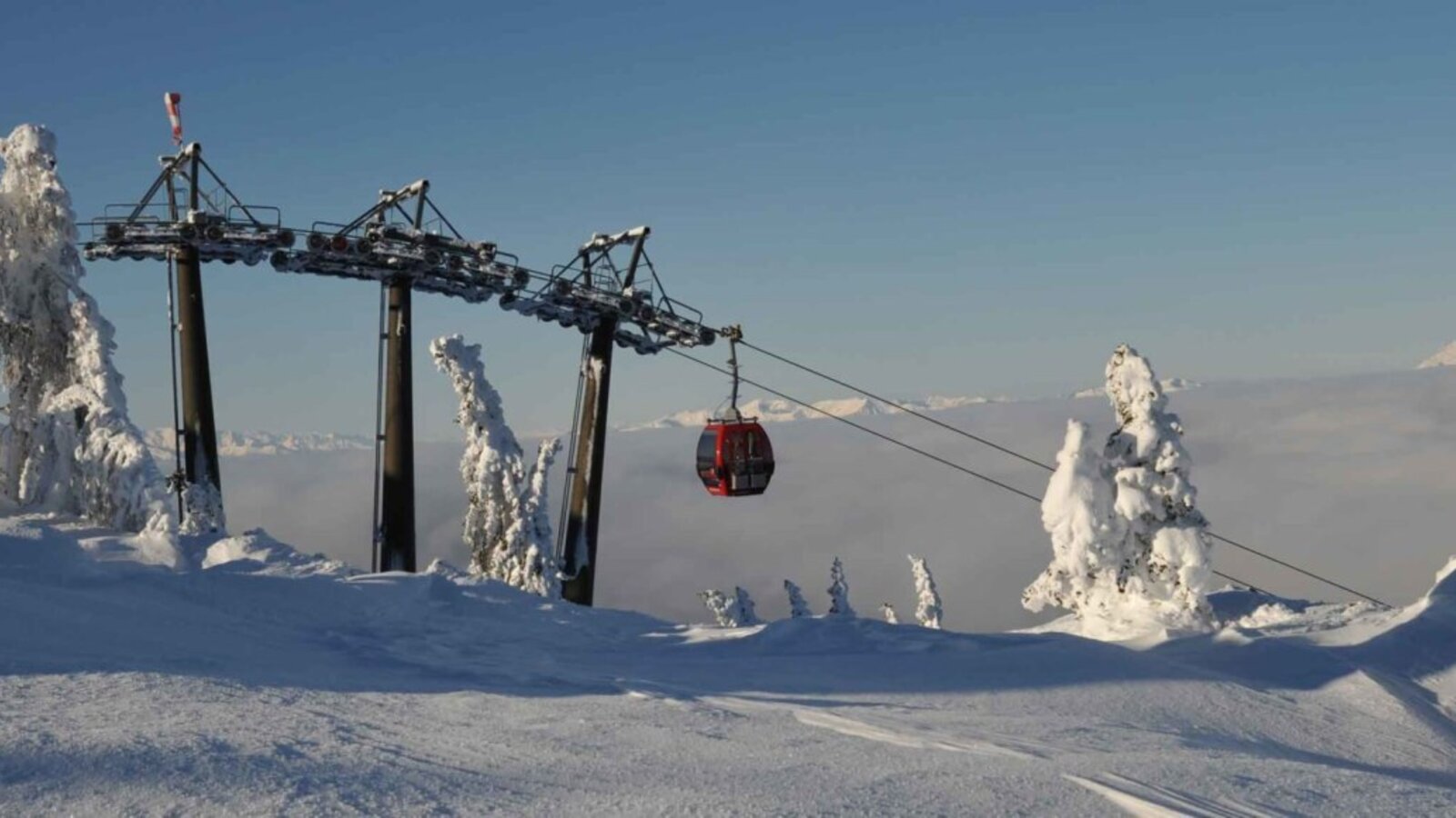 Gondelbahn in einer verschneiten Berglandschaft mit Blick auf die Wolkendecke.