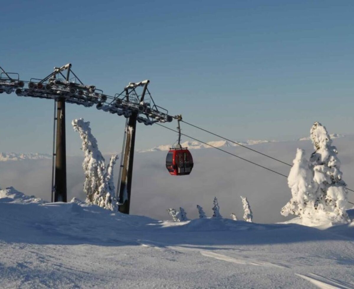 Gondelbahn in einer verschneiten Berglandschaft mit Blick auf die Wolkendecke.