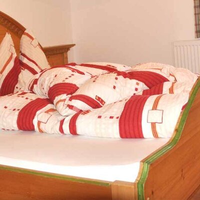 Schlafzimmer der Ferienwohnung mit Holzbett, rot-weiß gemusterter Bettwäsche und einem Waschbecken.