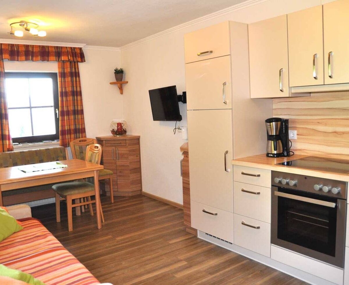 Wohnbereich der Ferienwohnung mit integrierter Küchenzeile, Essbereich mit Bank und Stühlen, Sofa und Fernseher.