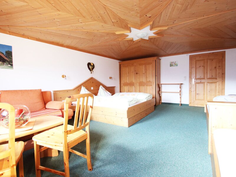 Vierbettzimmer mit  Sofa, Couchtisch, Holzmöbeln und einer Holzdecke.