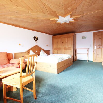 Vierbettzimmer mit  Sofa, Couchtisch, Holzmöbeln und einer Holzdecke.