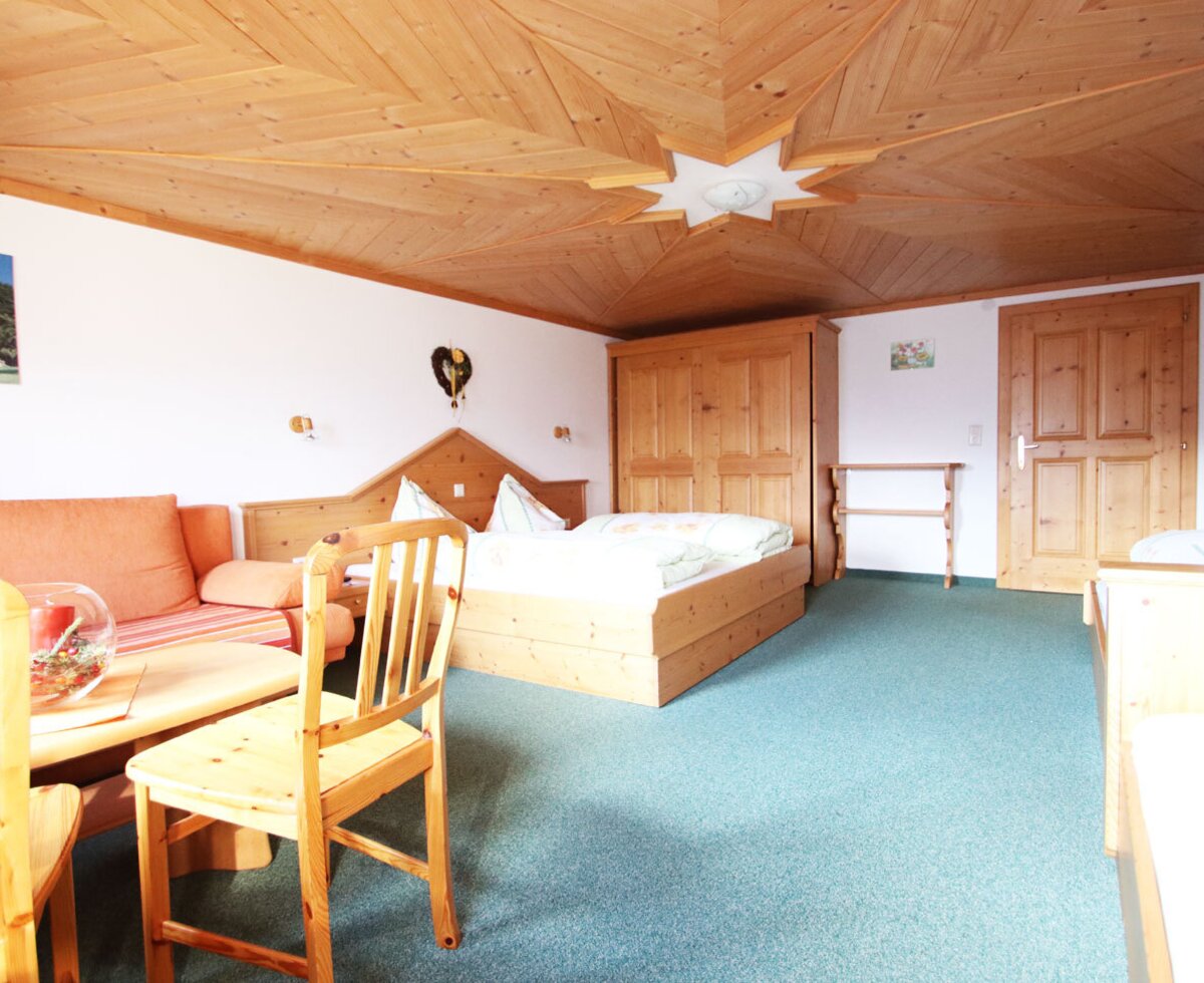 Vierbettzimmer mit  Sofa, Couchtisch, Holzmöbeln und einer Holzdecke.