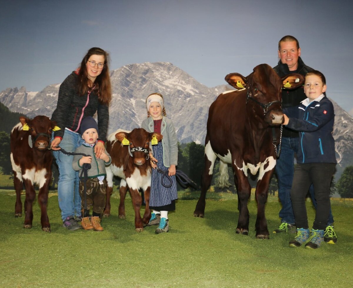 Die Gastgeberfamilie  mit ihren Kühen und Kälbern vor einer Bergkulisse.