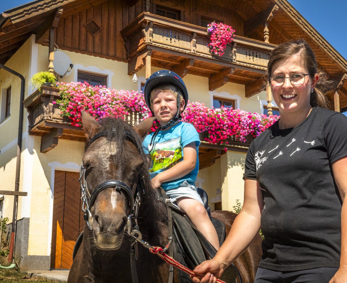 Die charmante Ferienwohnung mit blumengeschmückten Balkonen bietet ein familienfreundliches Erlebnis mit Ponyreiten vor dem Haus.
