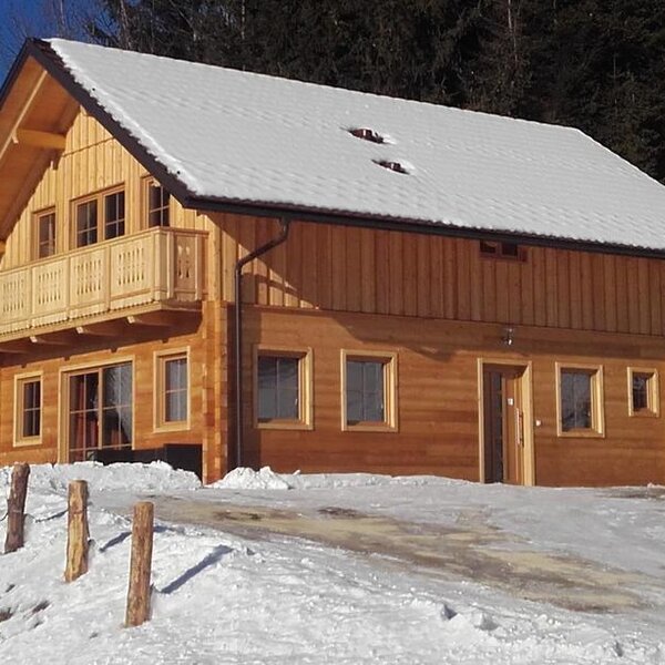 Das Bio Chalet Sonne in Holzbauweise mit Balkon, eingebettet in die winterliche Landschaft am Waldrand.