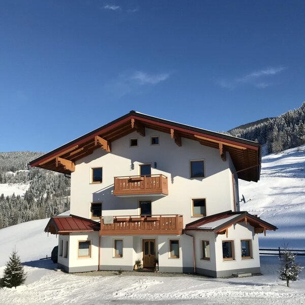 Der Bauernhof mit weißer Fassade, Holzbalkonen und verschneiter Berglandschaft.
