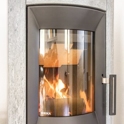 Kaminofen mit sichtbarem Feuer und Steinverkleidung im Bauernhof.