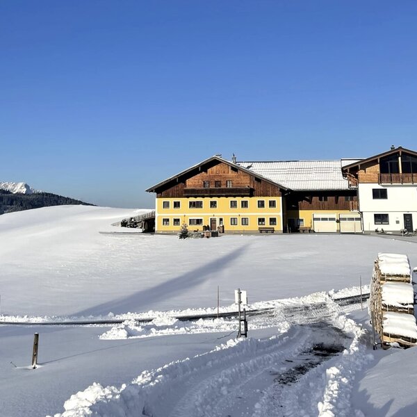 Der Bauernhof in seiner ruhigen Alleinlage, umgeben von einer tief verschneiten Landschaft und mit Bergkulisse.