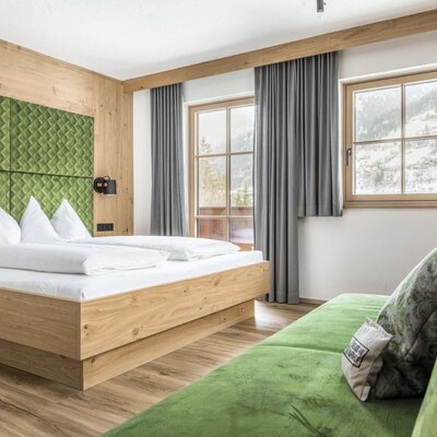 Doppelzimmer im Bauernhof mit Vollholzausstattung, grünem Kopfteil, Sofa und Bergblick.