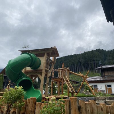 Spielplatz des Bauernhofs mit Holzspielturm, Rutsche und Schaukel.