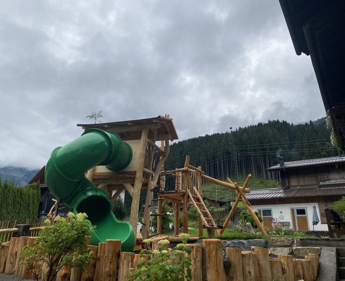 Spielplatz des Bauernhofs mit Holzspielturm, Rutsche und Schaukel.