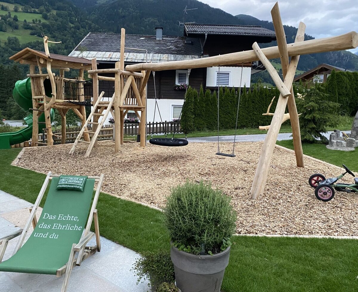 Der Spielplatz des Bauernhofs mit Holzturm, Rutsche und Schaukeln auf einem Untergrund aus Holzhackschnitzeln.