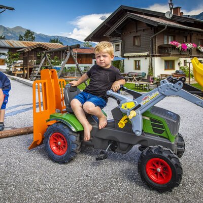 Zwei Kinder spielen mit einem Spielzeugtraktor und einer Spielzeugkettensäge auf dem Bauernhof.