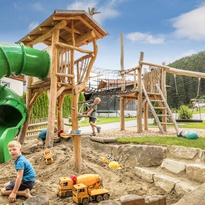 Der einladende Kinderspielplatz des Bauernhofs mit einer großen Rutsche, einer Sandkiste und Klettergerüsten aus Holz.