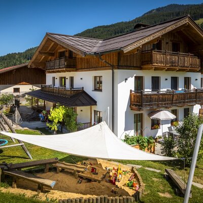 Der sonnige Außenbereich des Bauernhofs mit einem einladenden Kinderspielplatz samt Sandkiste und Schaukel.