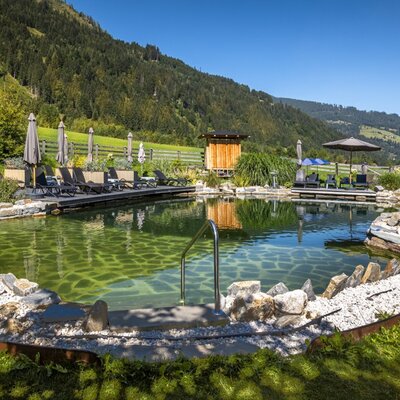 Der einladende Naturbadeteich des Bauernhofs mit einer sonnigen Liegewiese, gemütlichen Liegestühlen und herrlichem Bergblick.