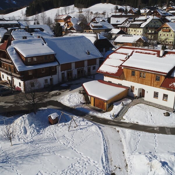 Der Bauernhof in einer schneebedeckten Dorfumgebung, mit einer Einfahrt und einem kleinen Kinderspielplatz.