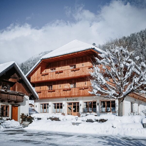 Außenansicht des Bauernhofs im Winter, mit Schnee auf dem Dach, den Balkonen und der umliegenden Landschaft.