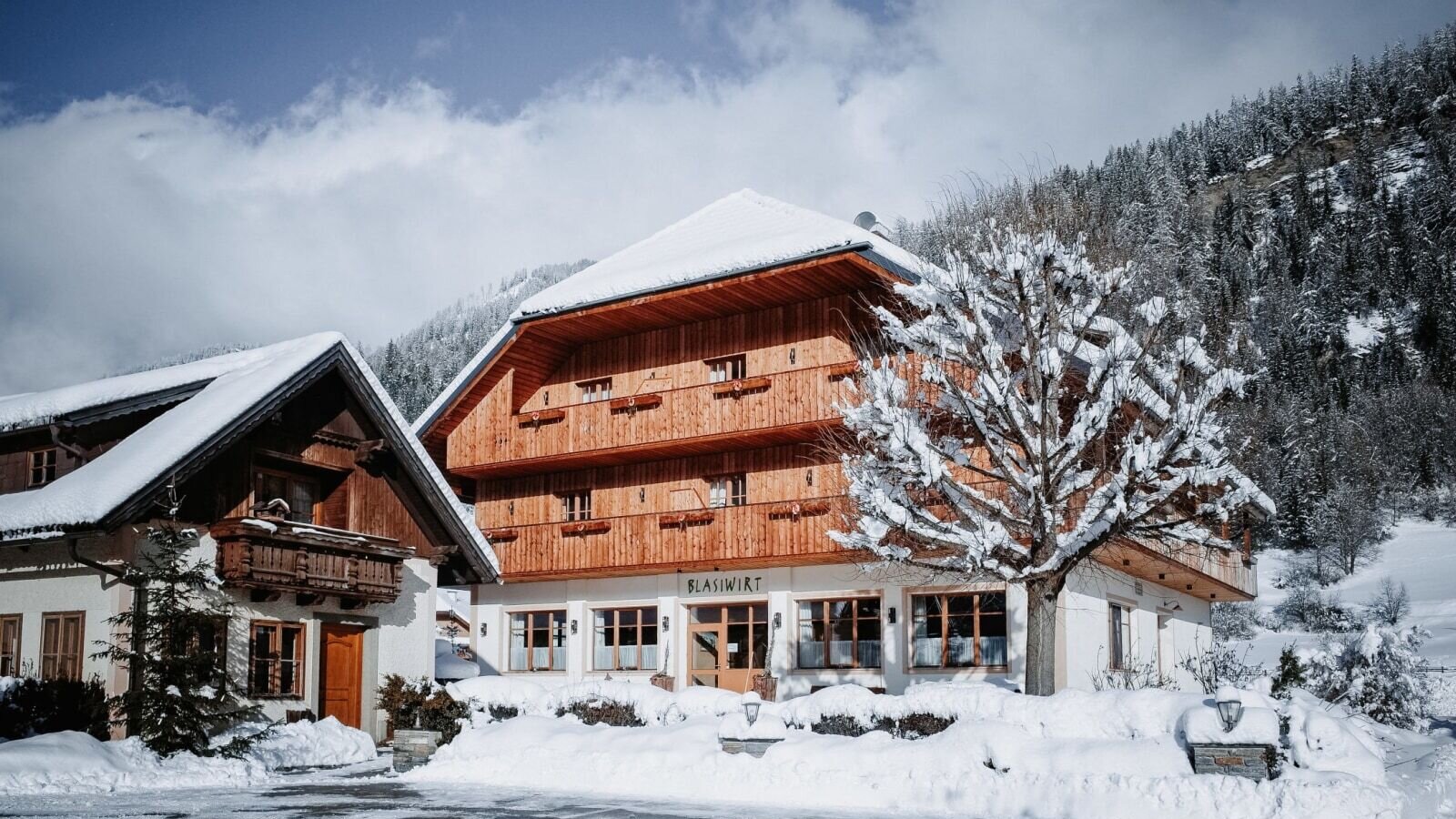 Außenansicht des Bauernhofs im Winter, mit Schnee auf dem Dach, den Balkonen und der umliegenden Landschaft.