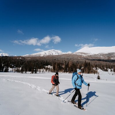Zwei Personen beim Schneeschuhwandern in der winterlichen Landschaft rund um den Bauernhof.