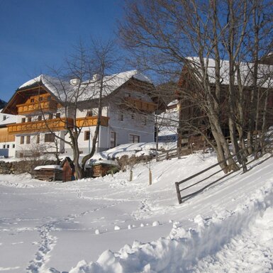 Der Bauernhof in verschneiter Winterlandschaft mit Holzbalkonen am Hauptgebäude.