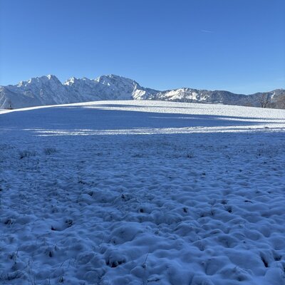 Verschneite Landschaft mit schneebedeckten Bergen im Hintergrund unter blauem Himmel, die den Bauernhof umgibt.