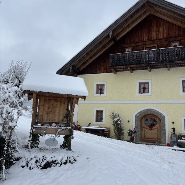 Der schneebedeckte Bauernhof mit Holzbalkon und einem traditionellen Eingangsbereich im Winter.