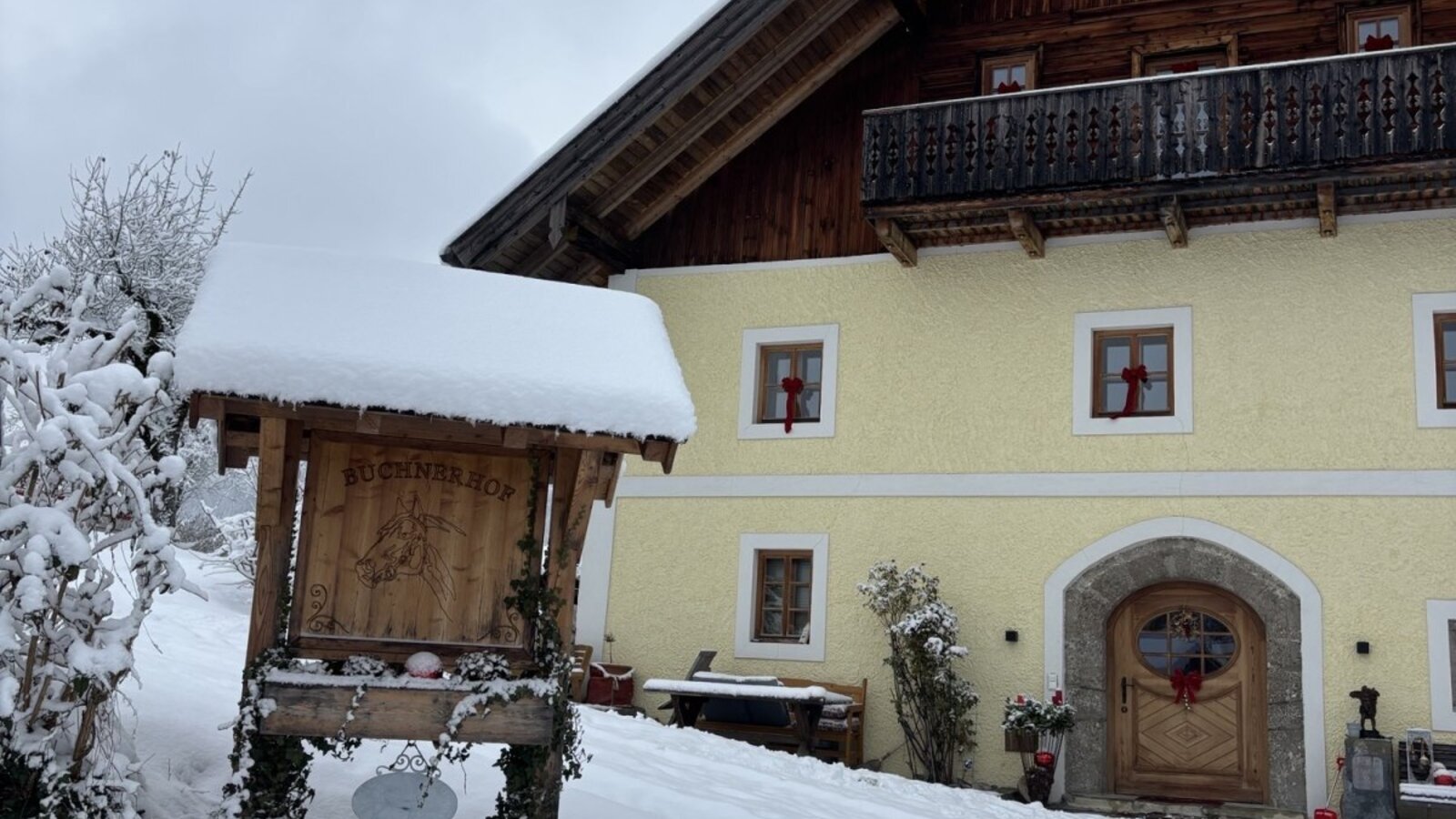 Der schneebedeckte Bauernhof mit Holzbalkon und einem traditionellen Eingangsbereich im Winter.