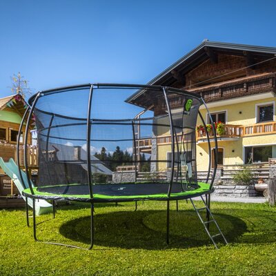 Einladender Spielbereich des Bauernhofs mit einem großen Trampolin, einem Holzspielhaus und einer Rutsche auf einer sonnigen Wiese.