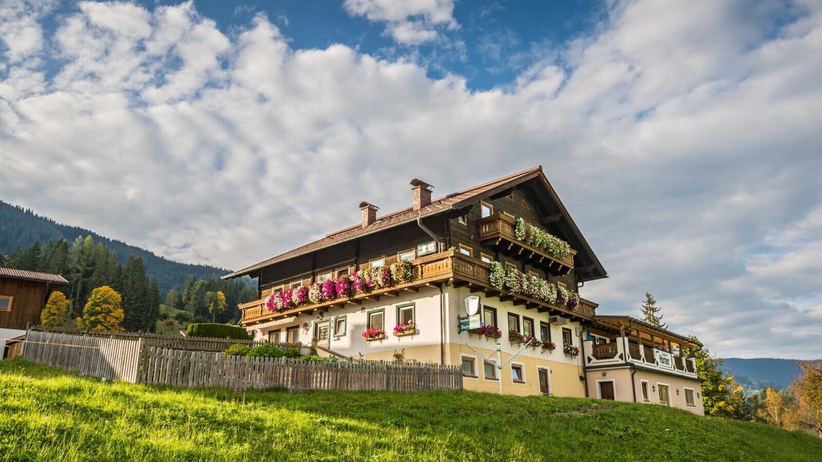 Außenansicht des Bed and Breakfast auf einem grünen Hügel mit Balkonen, die mit Blumen geschmückt sind.