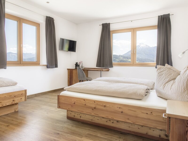 Schlafzimmer mit einem Doppelbett, einem Einzelbett, einem Schreibtisch und Bergblick.