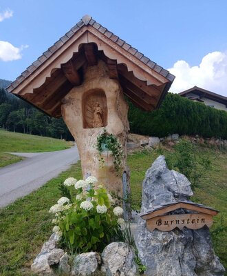 Ein liebevoll gestalteter Holzschrein und ein steinernes Namensschild empfangen Gäste am idyllischen Bauernhof.
