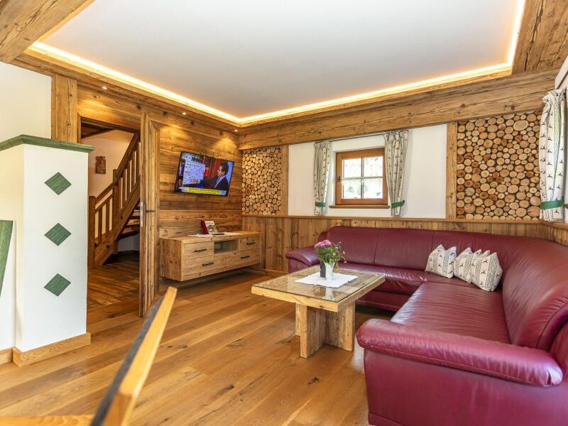 Wohnbereich im Bed and Breakfast mit rotem Ecksofa, Holzboden, TV und Zugang zur Treppe.