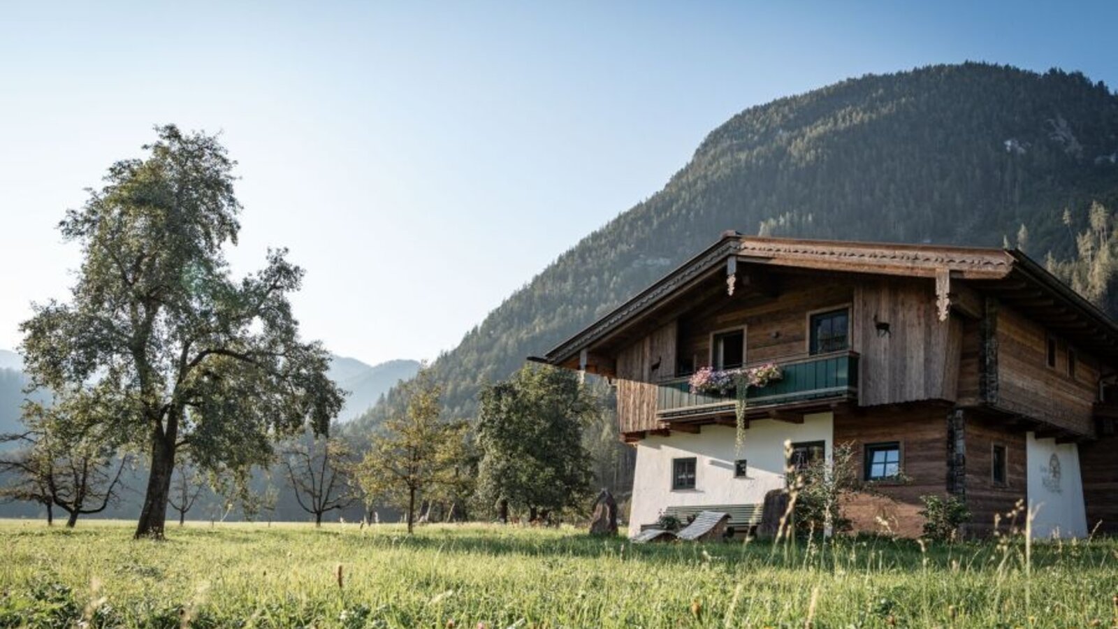 Außenansicht des Bed and Breakfast mit traditioneller Holzfassade, umgeben von einer Wiese und Bergen.