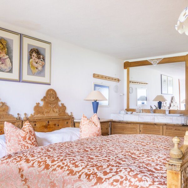Doppelzimmer im Ferienhaus mit geschnitztem Holzbett, gemusterter Bettwäsche und einem Waschtisch mit Spiegel.