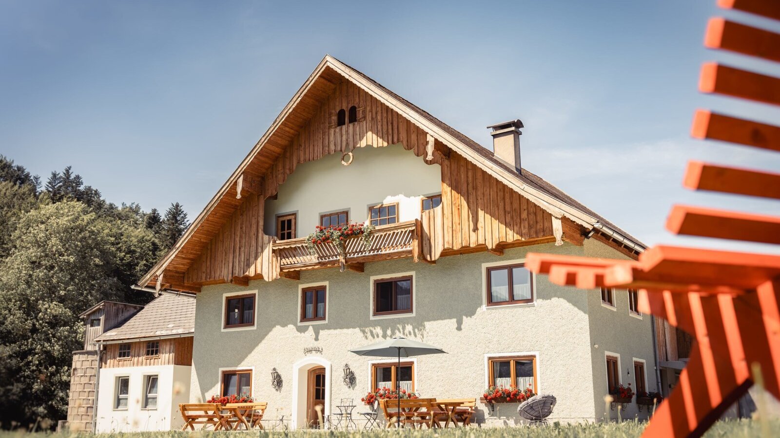 Der Bauernhof von außen, ausgestattet mit einem Balkon, Blumenkästen und einem Sitzbereich mit Tischen und Bänken.