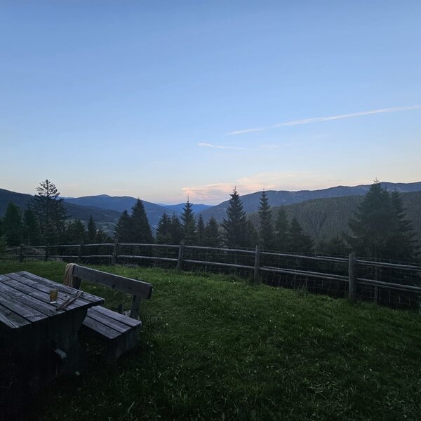 Außenbereich des Bed and Breakfast mit Holztisch, Bänken und Blick auf die Berge und Wälder.