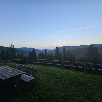 Außenbereich des Bed and Breakfast mit Holztisch, Bänken und Blick auf die Berge und Wälder.
