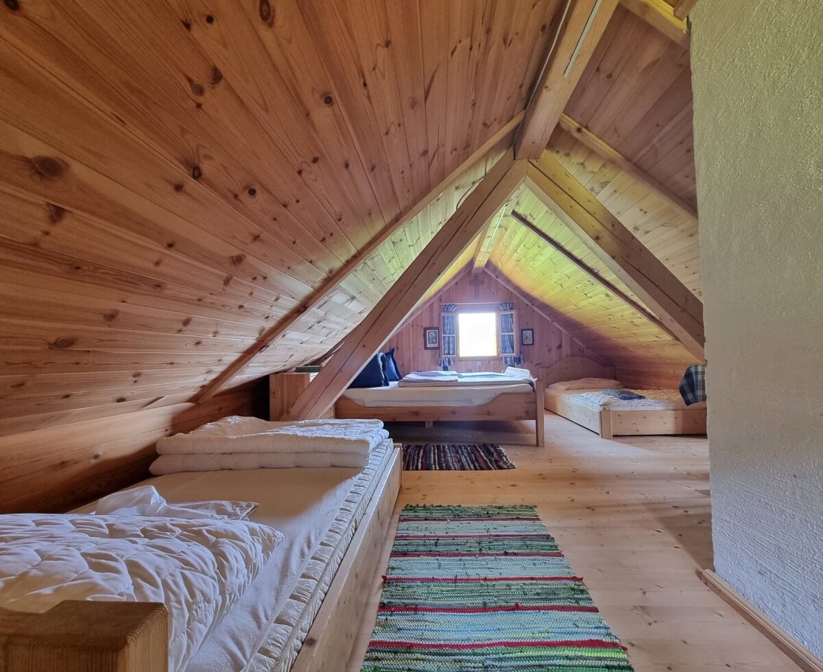 Dachgeschoss-Schlafzimmer der Almhütte mit mehreren Betten, Holzwänden und einem Fenster.