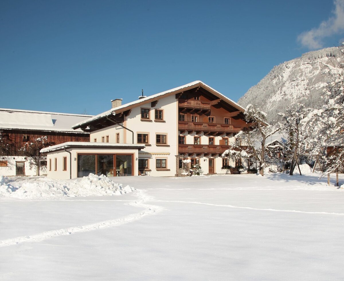 Der Bauernhof im Winter mit schneebedecktem Garten, Kinderspielplatz und Bergblick.