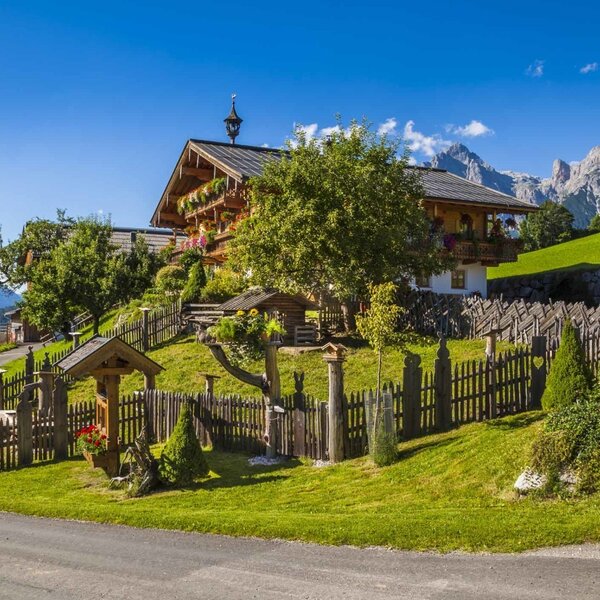 Der Bauernhof auf einer grünen Anhöhe mit traditionellem Holzzaun und Bergblick.
