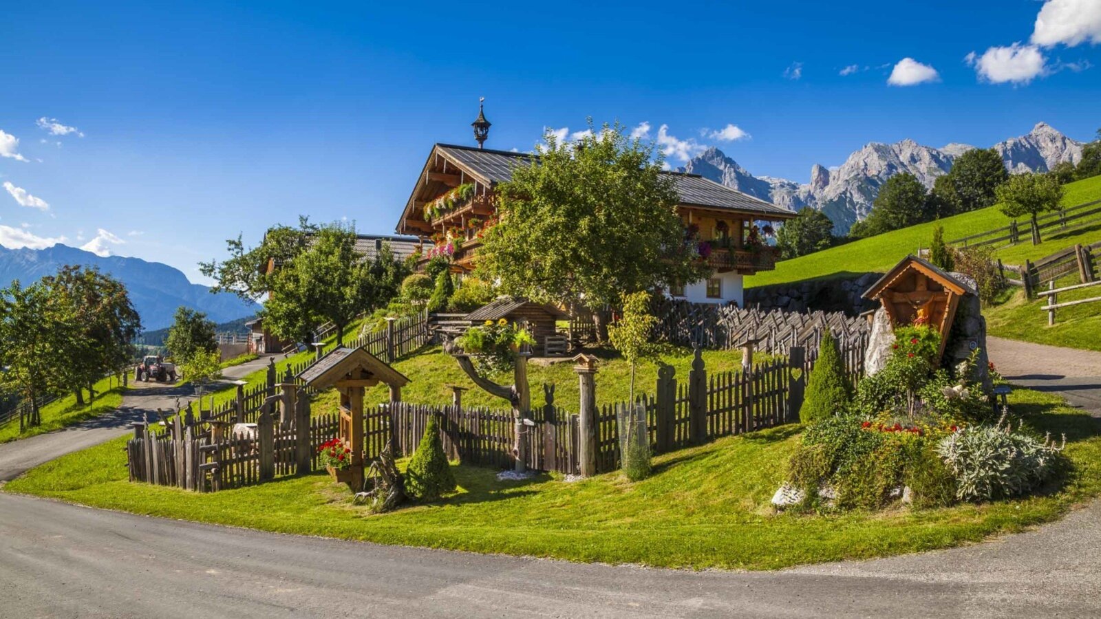 Der Bauernhof auf einer grünen Anhöhe mit traditionellem Holzzaun und Bergblick.