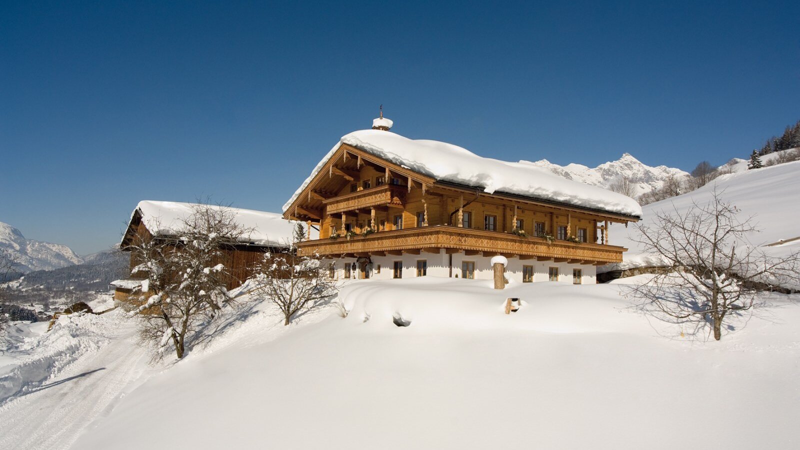 Der Bauernhof mit Holzbalkonen und schneebedecktem Dach, eingebettet in eine winterliche Berglandschaft.