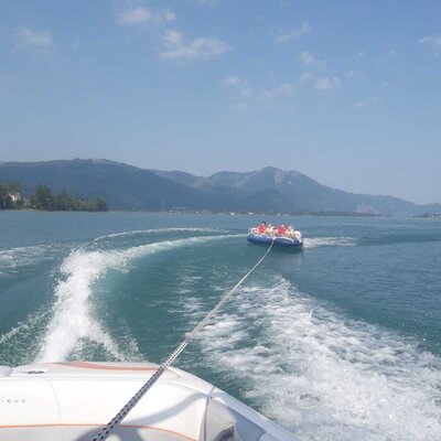 Wassersport mit einem gezogenen Schlauchboot auf dem See vor einer Berglandschaft.
