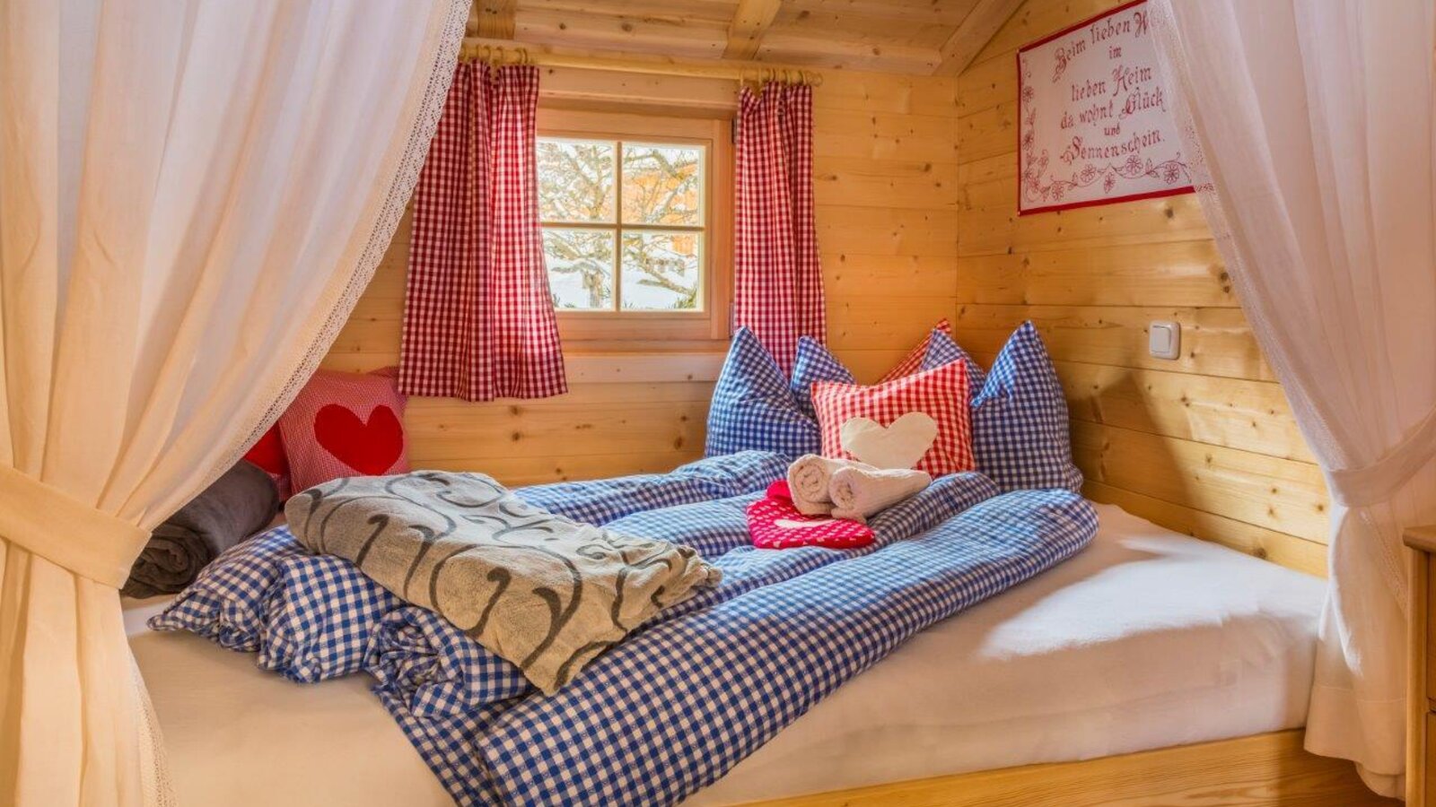 Einzelbett im Bed and Breakfast mit blau-weiß karierter Bettwäsche, Holzwänden, einem Fenster mit rot-weiß karierten Vorhängen und einem Betthimmel.