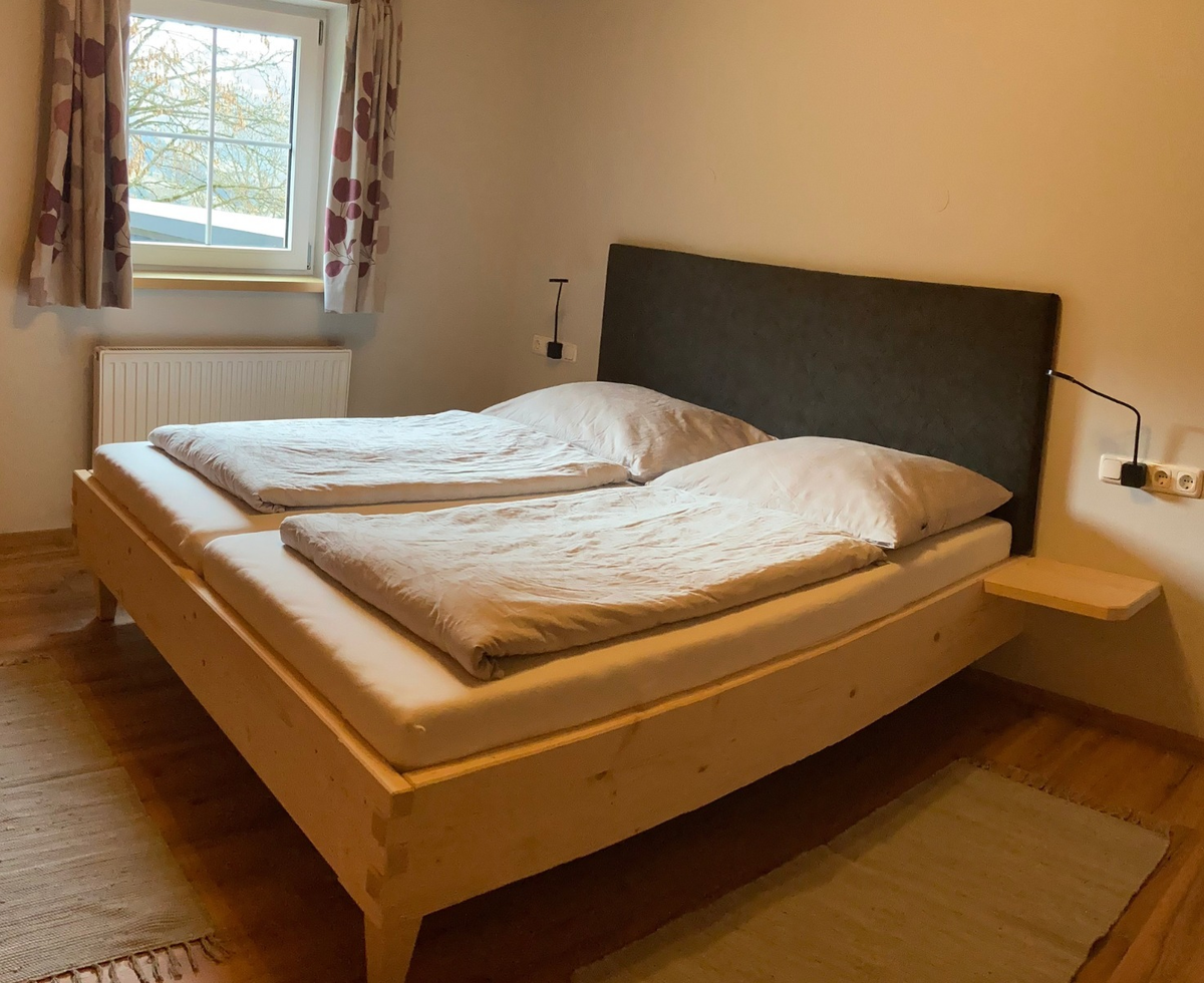 Schlafzimmer der Alm mit Doppelbett, Holzbettrahmen, Leselampen und Fenster.